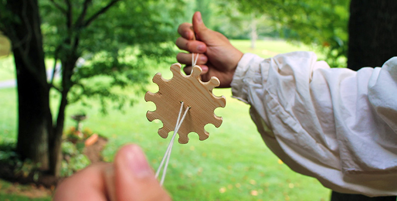 A person holds up a toy made of a notched disk and a string.