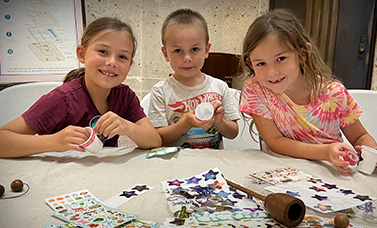 Three smiling children at a table making a cup and ball toy