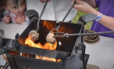 People making camp bread with dough cooked over an open flame.