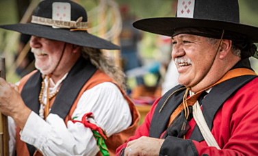 Two living history reenactors wearing hats with playing cards in the headband.