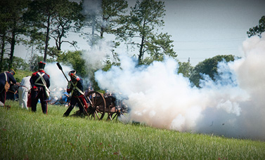 Living history re-enactors representing Mexican artillerymen firing a replica cannon.