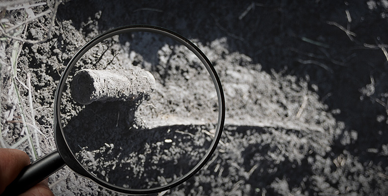 A magnifying glass inspecting an old tool encrusted with dirt.