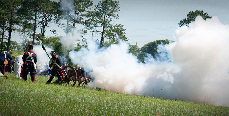 Living history re-enactors representing Mexican artillerymen firing a replica cannon.