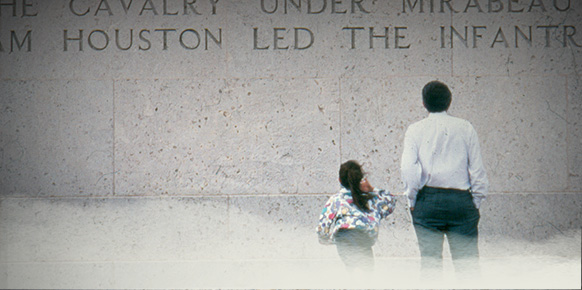 A father and daughter looking up at a wall of the San Jacinto Monument