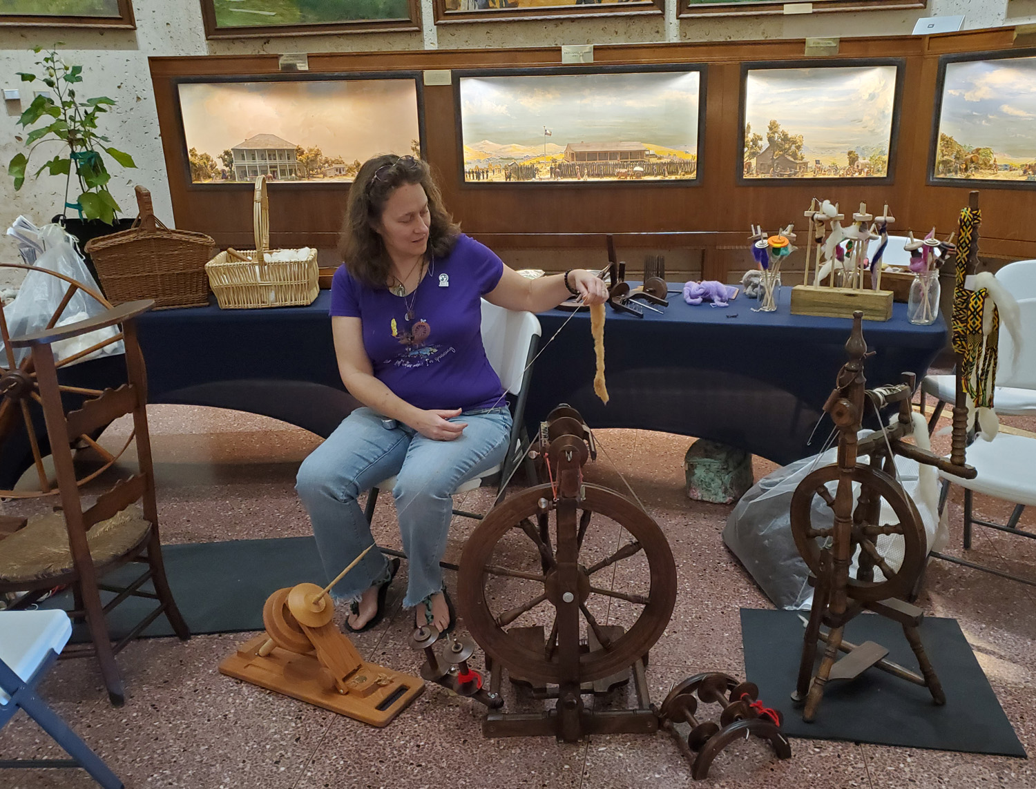 A woman sits amid spinning wheels spinning yarn inside the San Jacinto Museum.