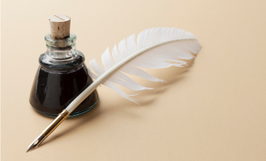 A quill pen rests against the side of a glass bottle of ink.