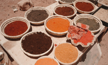 Eleven baskets of colorful powders sit on a table.