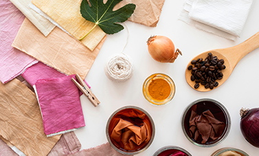 Pieces of colorful fabric on the right, with vegetables, a leaf, and powders used as dyes on the right.