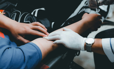 A gloved hand holds a gauze pad on a blood donor's arm.