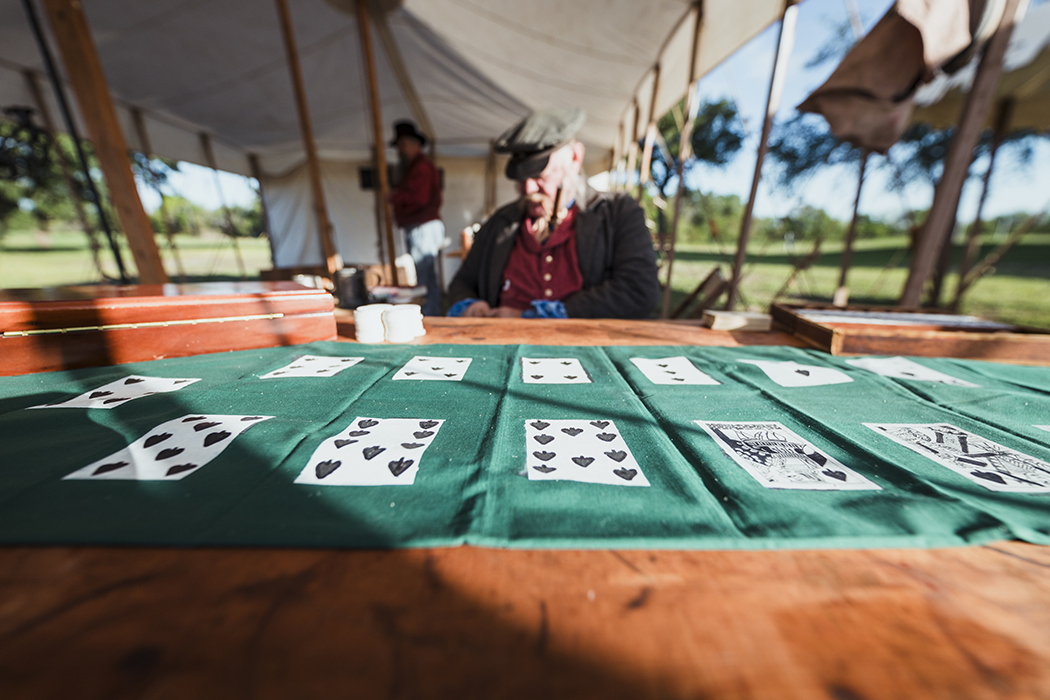 A cloth showing playing cards is laid out on a table in a tent, with a reenactor behind it