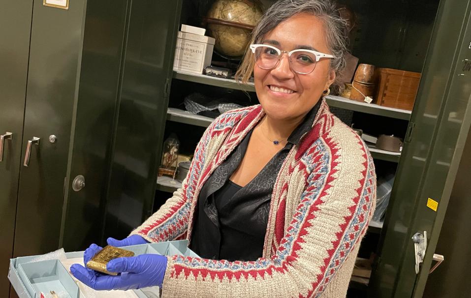 A curator holds a small artifact in a gloved hand.