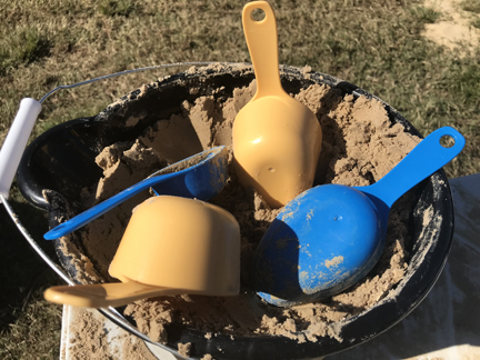 Four plastic scoops sit on top of a bucket of sand