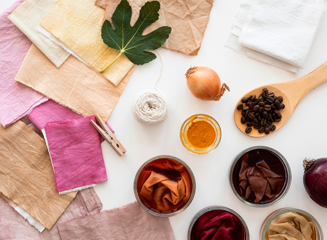 Pieces of colorful fabric on the right, with vegetables, a leaf, and powders used as dyes on the right.
