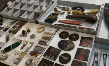 Artifacts including small paintings and boxes are laid out on trays. on