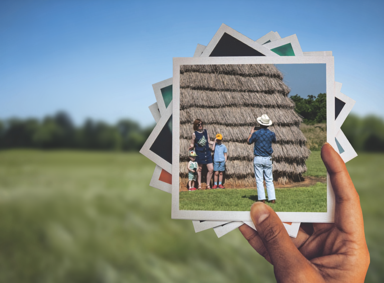 A hand holds up a stack of snapshots.