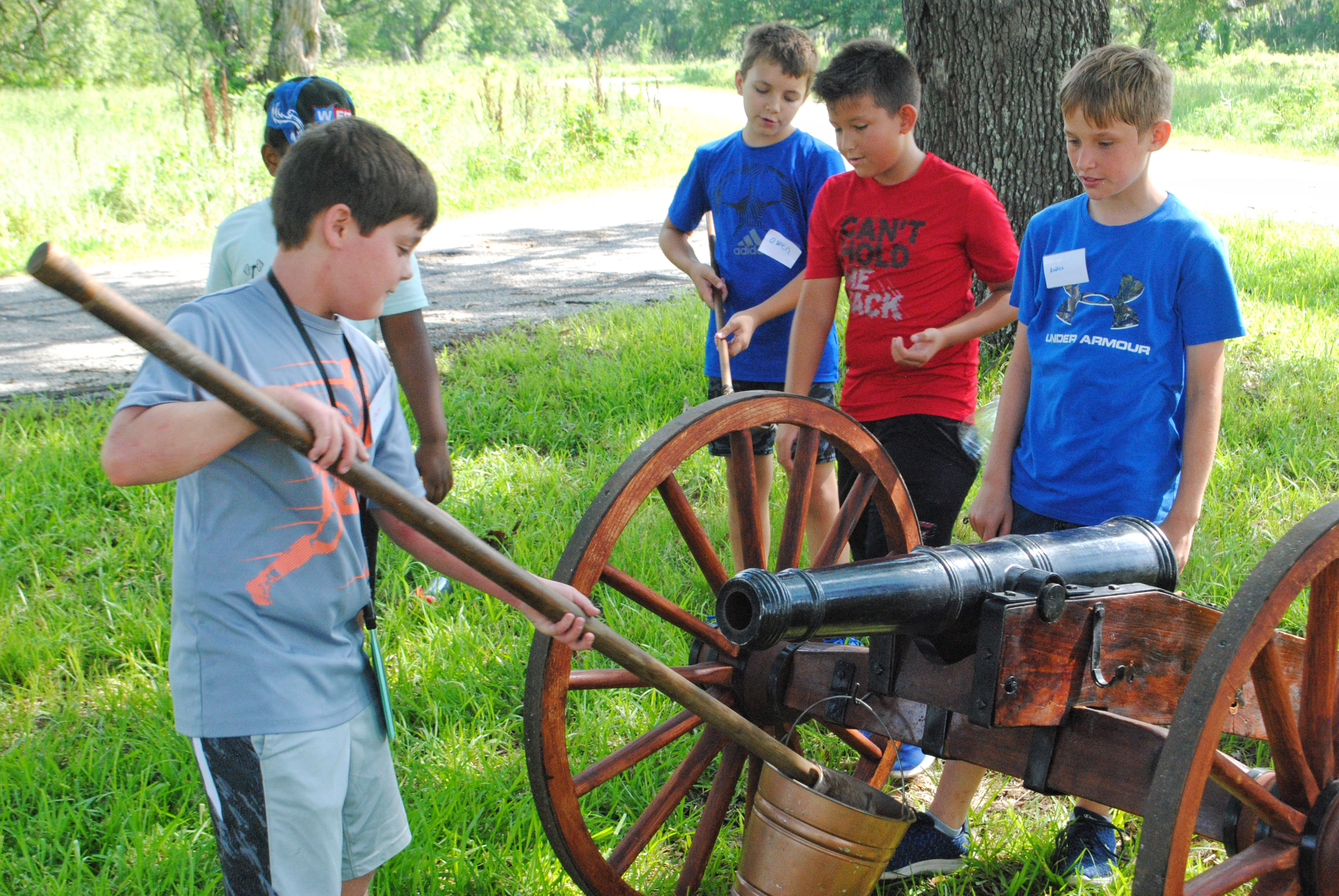 A boy swabs out a cannon while four other boys watch.