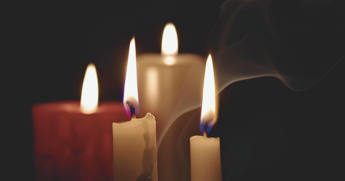 Four candle burn against a dark background, with a wisp of smoke.