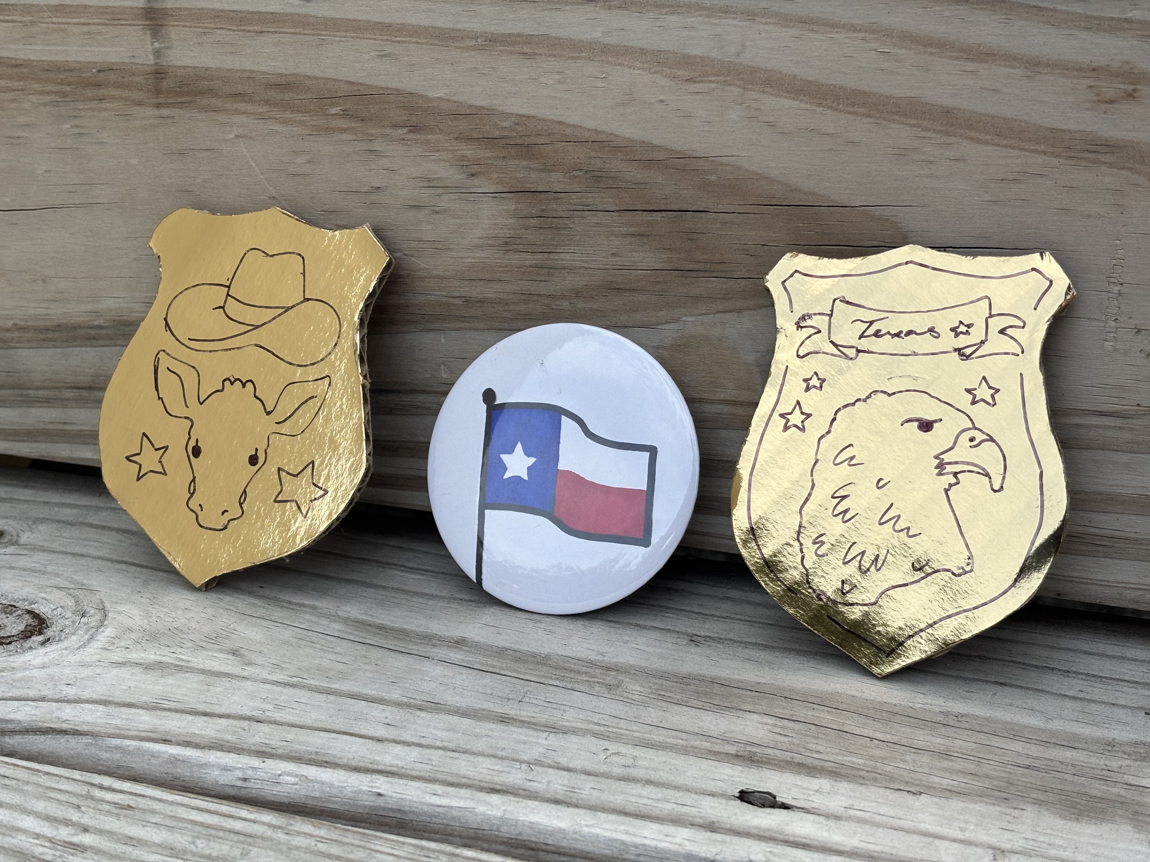 Two gold-colored shilds with symbols in black, and a button with a Texas flag.