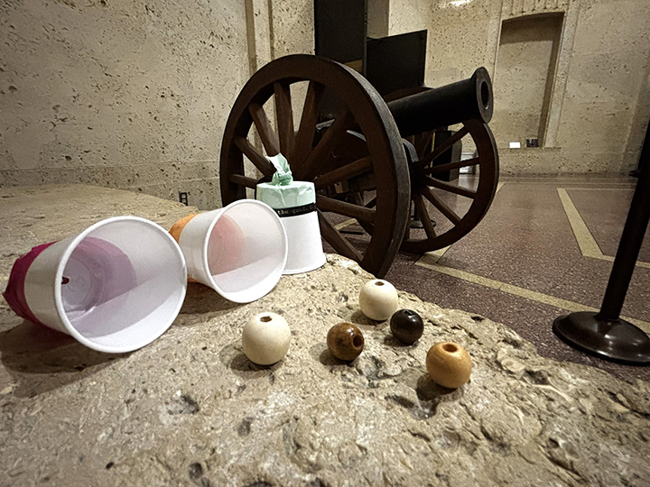 "Cannons" made of plastic cups sit on a ledge in front of a cannon.