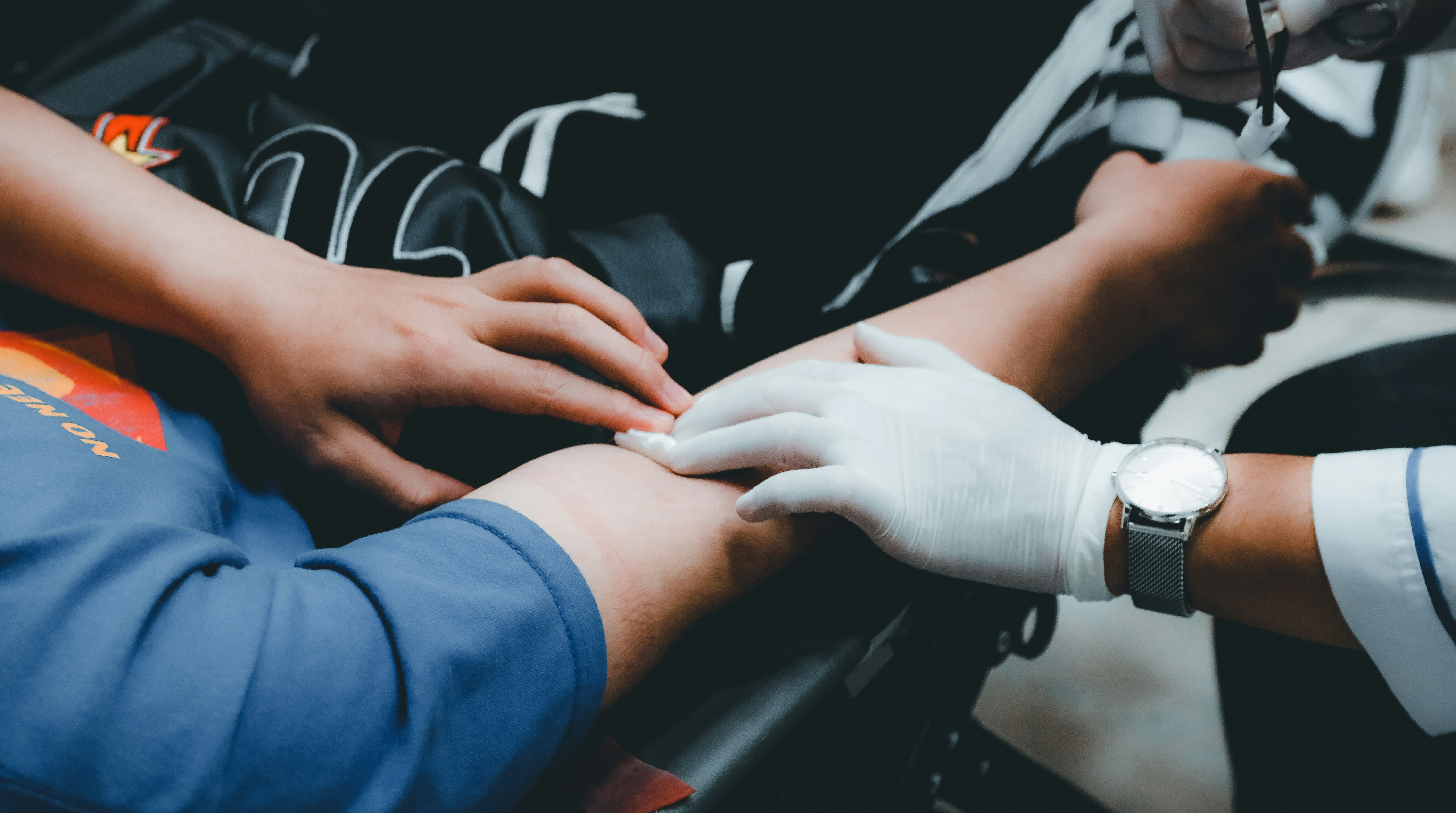 A gloved hand holds a gause pad on the arm of a blood donor