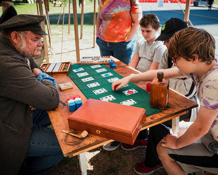 A man in 1830s clothing plays a card game with a boy