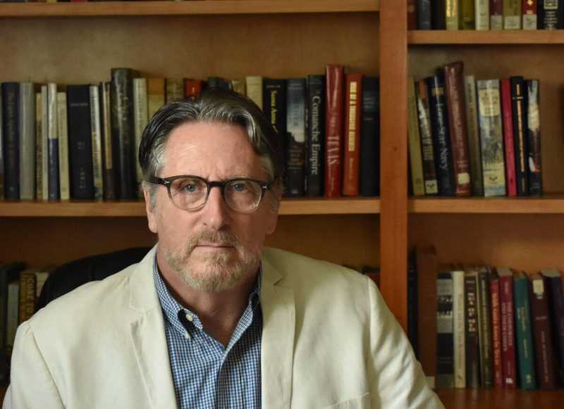 Head and shoulders shot of Sam Haynes in front of bookshelves.