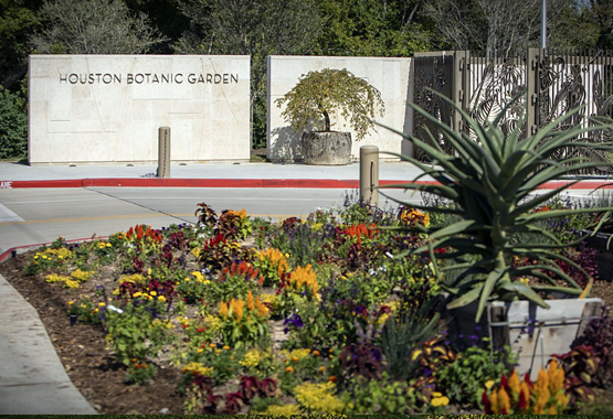 Entrance to the Houston Botanical Garden with flower beds and sign.