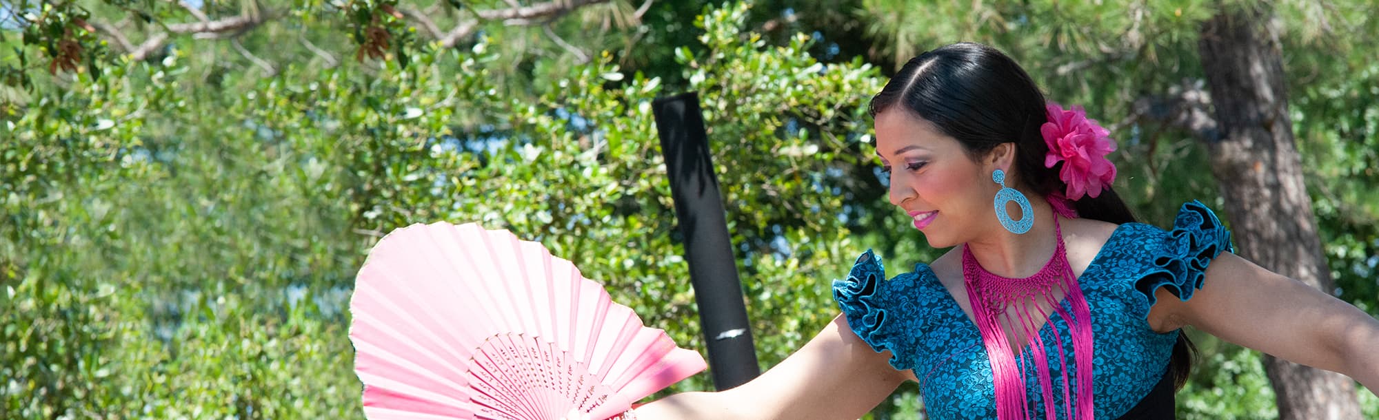 A woman dressed in traditional Mexican garb dancing with a pink fan