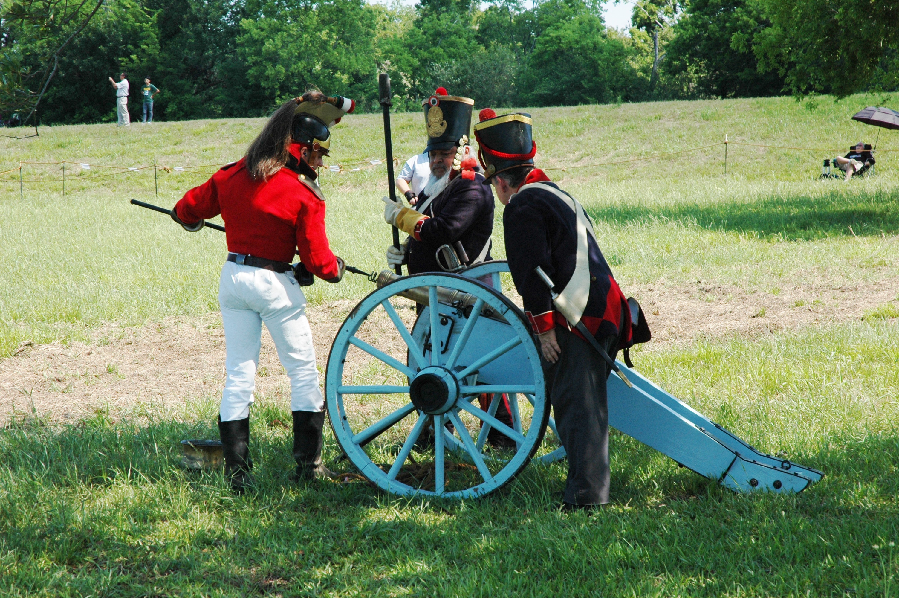 Three men wearing the uniforms of the 1830s Mexican army load a cannon.