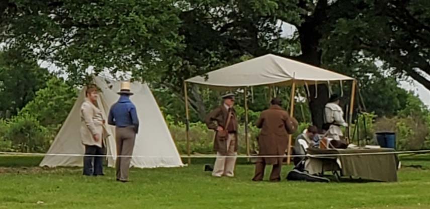 Reenactors presenting the Texas Revolution of 1836 talk together in front of canvas tents